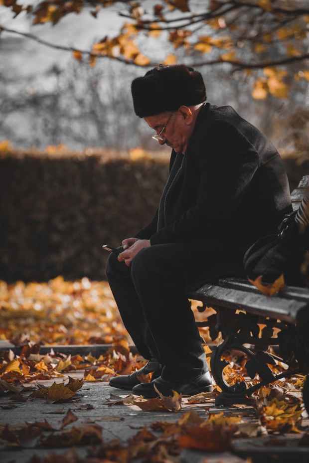 photo of man sitting on wooden bench while using cellphone